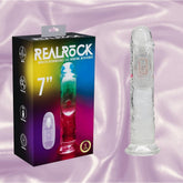 The RealRock Wireless Rechargeable LED Vibrating 7" by Shots America is shown with its vibrant packaging and a white remote, displayed on a silky light pink background, combining realistic style with wireless convenience.